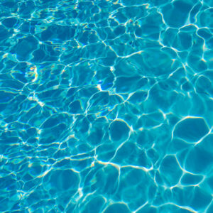 Sunlight glints off the clear blue water of a finished pool finished with premium stone edging.