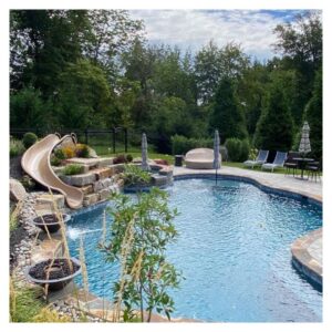 A fun swimming pool with a slide, surrounded by green trees and potted plants.