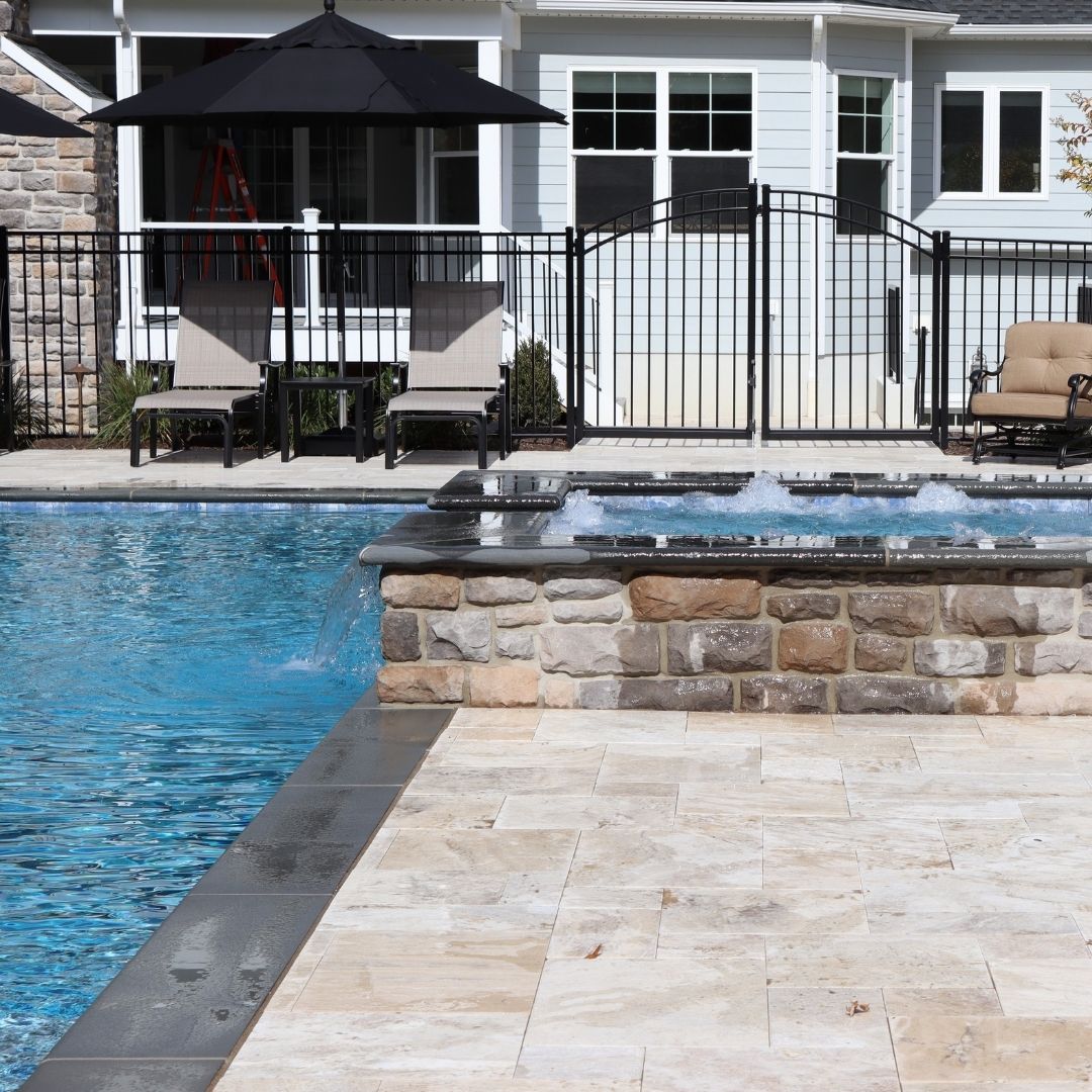 Raised stone hot tub spilling water into blue pool.