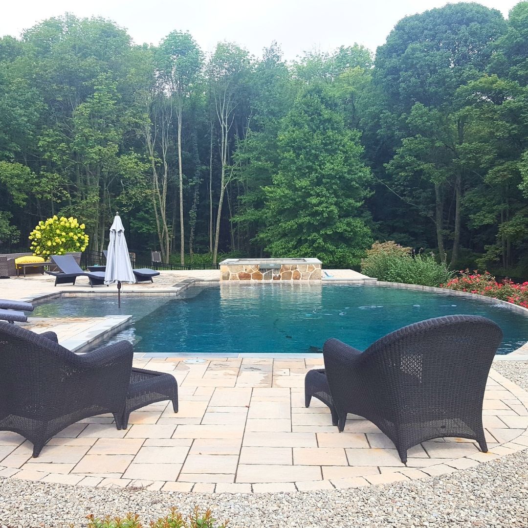 Dark blue pool and patio chairs backed by woods.