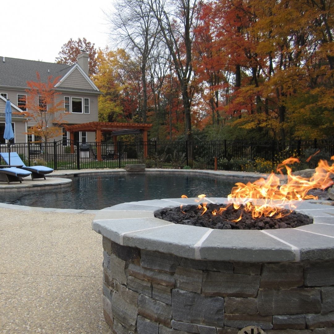 Stone fire pit burning near pool with autumn trees