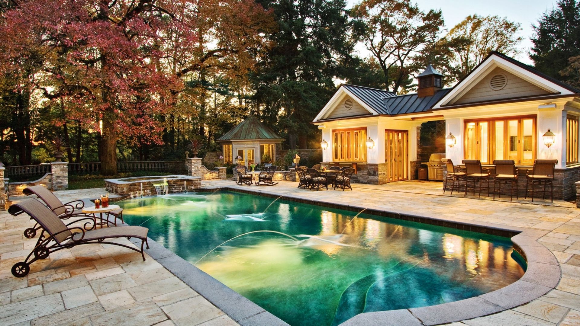 Multi-Seasonal Backyard hero Illuminated luxury pool and pool house at dusk.