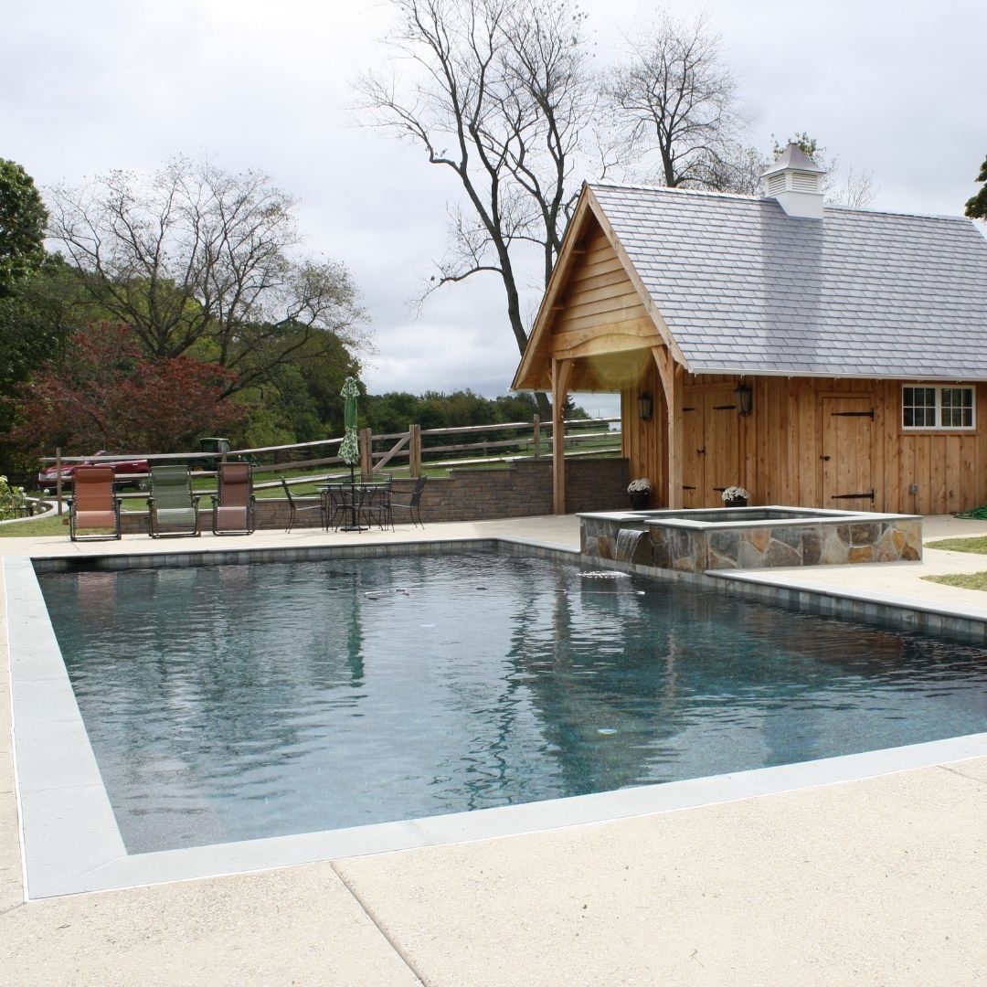 Dark finish swimming pool and spa near wooden pool house.