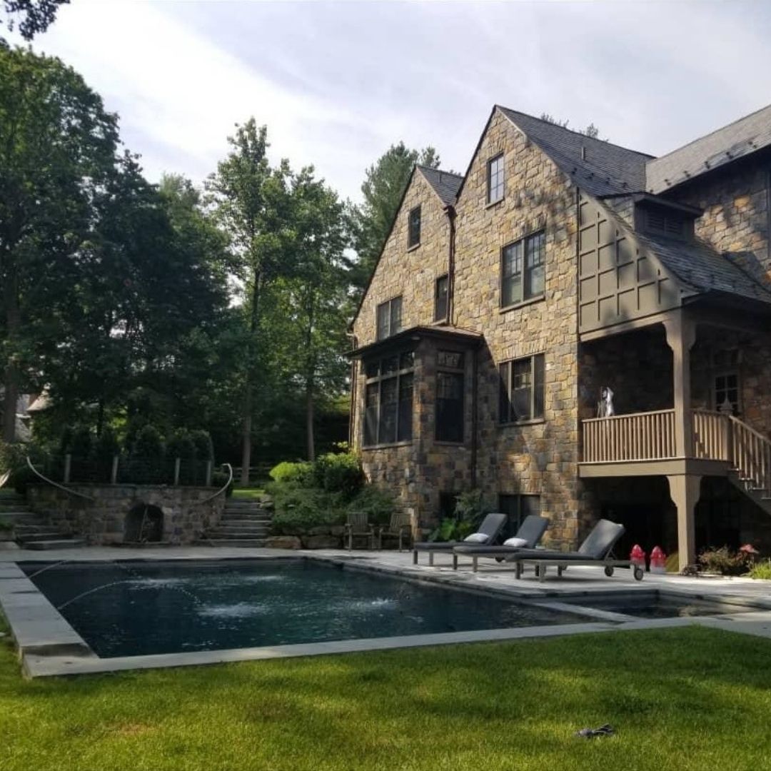 Dark bottom swimming pool with fountains behind stone estate home